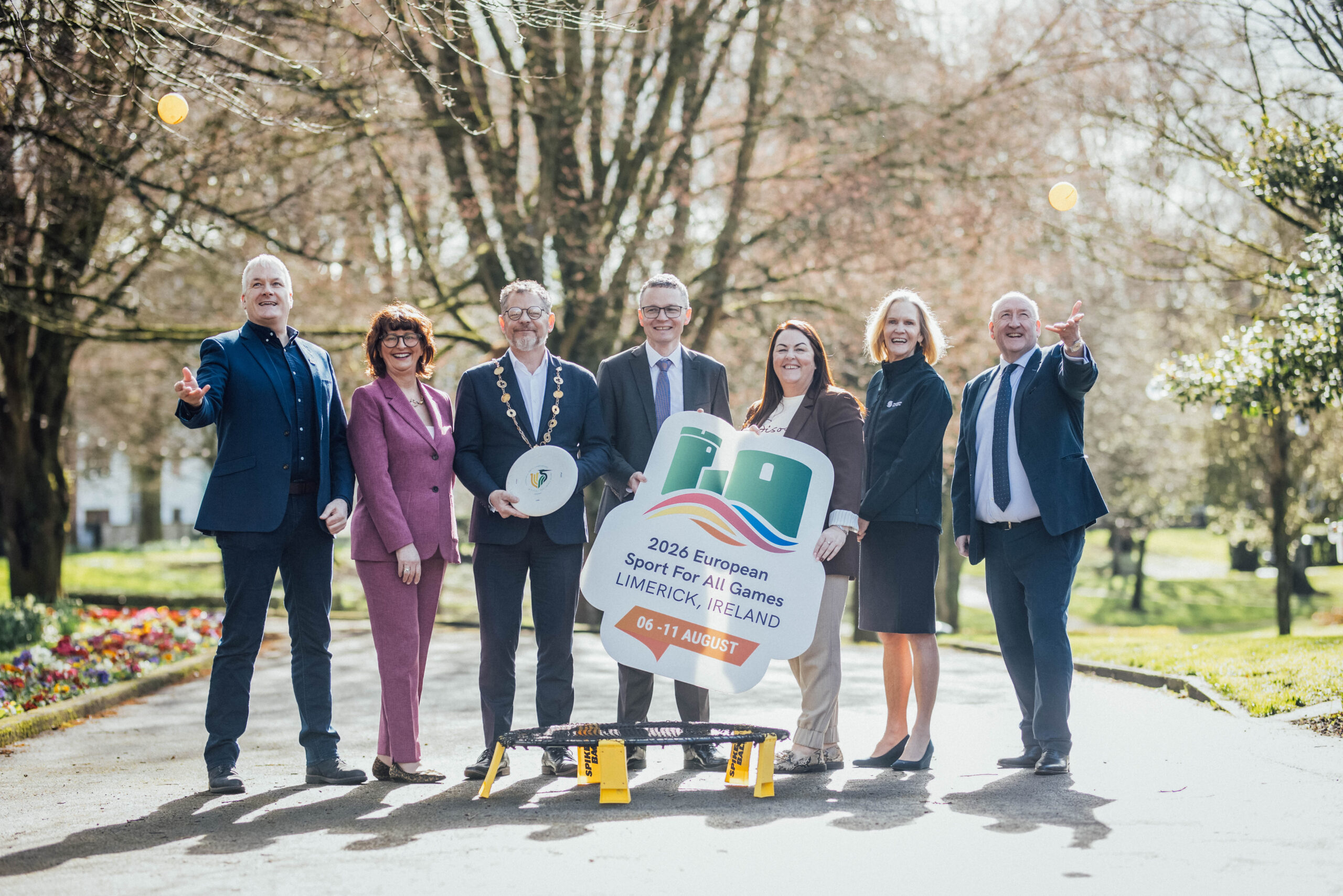 Three women and four men holding a sign in a park all smiling
