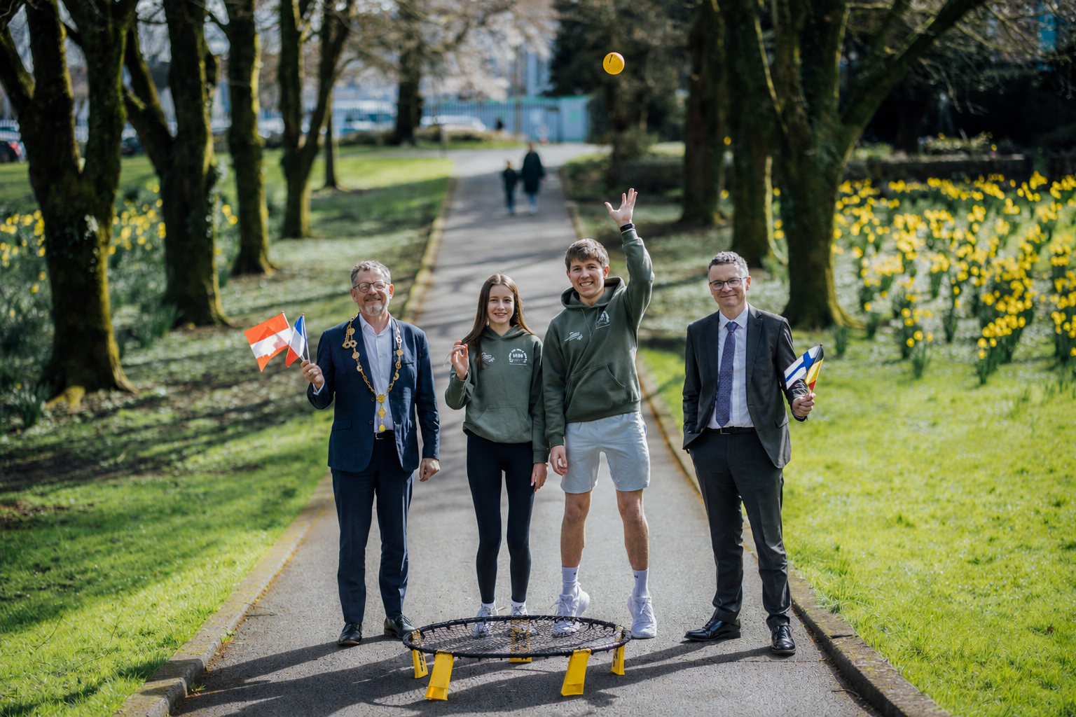 Hands up Volunteers wanted for ESFAG two young people in a city park with a mayor and minister holding small european flags