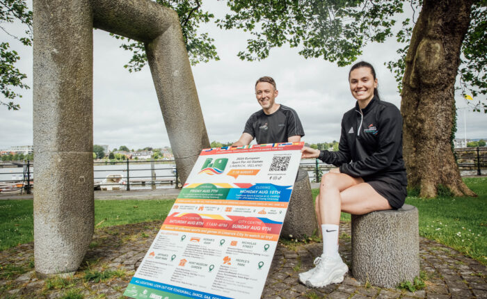 man and woman sitting in park holding a large poster sign of a festival programme details