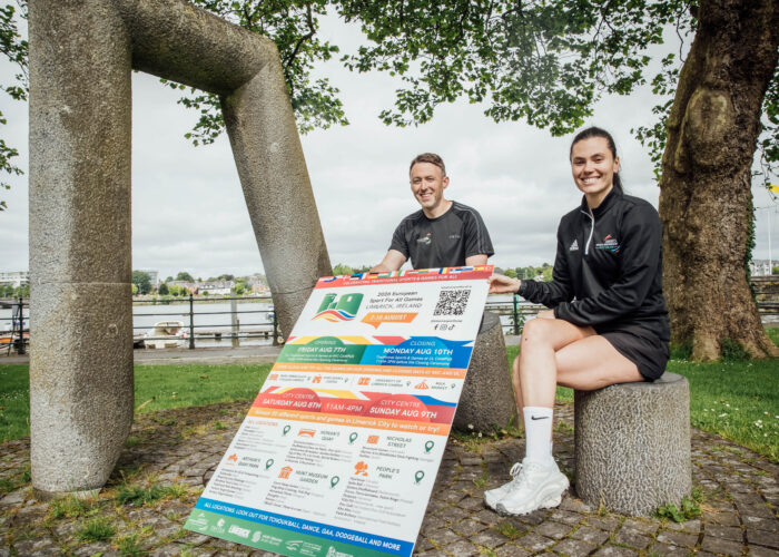 man and woman sitting in park holding a large poster sign of a festival programme details